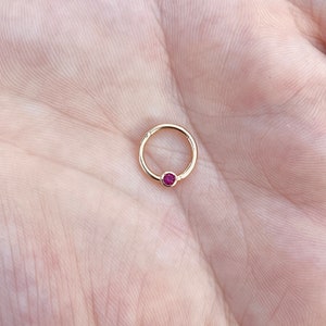 May include: Gold hoop earring with a small, round, pink gemstone.