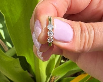 May include: A gold band ring with three round clear stones set in a row.