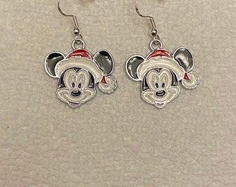 May include: A pair of silver-toned dangle earrings featuring Mickey Mouse wearing a Santa hat. The earrings have a black and white face with a red and white Santa hat. The earrings have a fish hook style closure.
