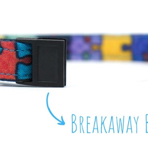 May include: A colourful cat collar with a jigsaw puzzle pattern and a breakaway buckle. The collar has a bell attached.