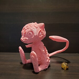 Op de afbeelding: Een roze 3D-geprint beeldje van een Pokemon-personage, met ingewikkelde details en een gekrulde staart. Het beeldje staat op een houten oppervlak.