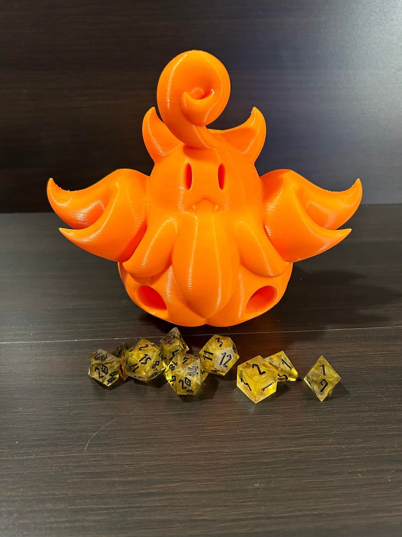 May include: An orange 3D-printed creature with a curly top and tentacle-like appendages. Several yellow and black dice are arranged in front of the creature, suitable for tabletop gaming.