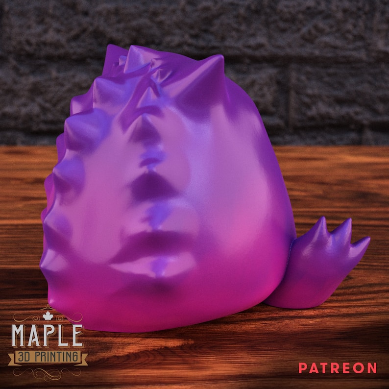 May include: A purple and pink 3D printed figurine of a spiky, round creature with a tail. The figurine is sitting on a wooden surface.