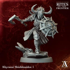 Puede incluir: Figura en miniatura gris de Khyrana Shieldmaiden 1, empuñando un hacha de batalla y un escudo. El escudo presenta un diseño de calavera. La figura lleva armadura y un casco con cuernos. El texto "Hordes of Wrath Rites of the Frontier" y "A Games" son visibles.