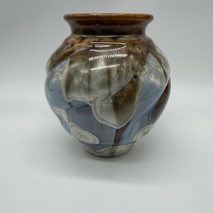 May include: A bulbous ceramic vase featuring a crystalline glaze with a glossy finish. The surface displays a blend of deep brown at the rim and base, transitioning into a soft blue and grey body with distinct white, flower-like crystal patterns.
