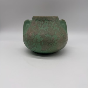 May include: A white ceramic mug with a black handle and the text "But First, Coffee" in a bold, black font. The mug is set against a blurred background, suggesting a cozy setting.
