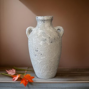 May include: A white ceramic vase with a textured surface and two handles. The vase is sitting on a wooden surface.