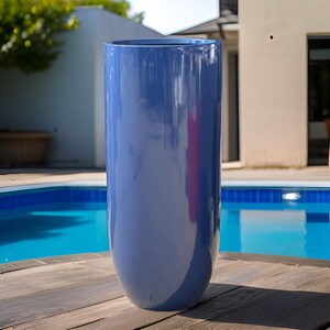 May include: A tall, cylindrical planter with a smooth, glossy finish in a deep blue color. The vessel features a simple, uniform shape with a wide, open top and a slightly tapered base, reflecting light across its polished, reflective surface.