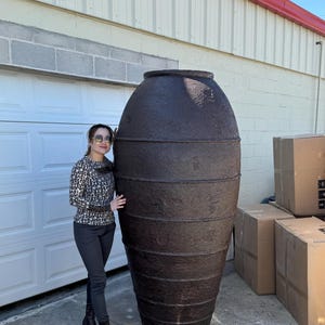 May include: A large, dark brown, ceramic planter with a rounded, oval shape. The planter has a textured surface and is decorated with horizontal bands.