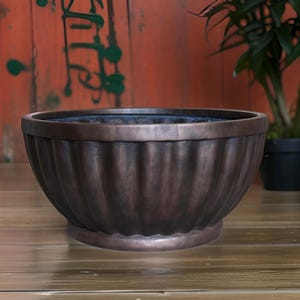 May include: A large, dark brown, round planter with a fluted design. The planter is made of a durable material and has a smooth, glossy finish.