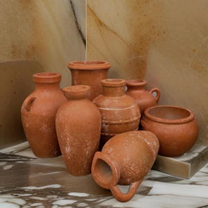 May include: A collection of seven terracotta pots of varying sizes and shapes. The pots are all a reddish-brown color and have a rustic, handmade appearance.
