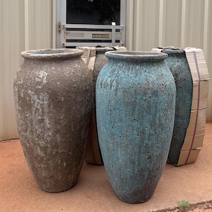 May include: Three large, tall, tapered floor planters with a rough, weathered texture. One planter is a muted brown, while the other two feature a vibrant, oxidized turquoise finish with dark brown undertones. Each vessel has a wide, rounded rim.