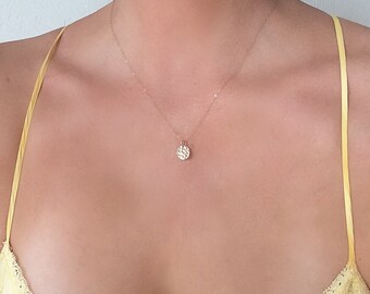 Peut inclure: Un délicat collier en or avec un petit pendentif circulaire texturé. Le pendentif est suspendu à une fine chaîne, créant un look minimaliste et élégant. Le collier est présenté sur un fond clair.