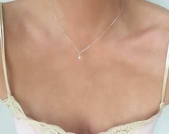 Puede incluir: Un delicado collar de cadena de plata con un pequeño colgante de perla.