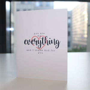 May include: A white card with a pink heart and black text that reads "You are my everything and I thank God for you."