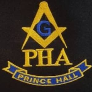 May include: A black and gold embroidered patch with a compass and square design. The compass has a blue "G" in the center. The words "PHA" and "PRINCE HALL" are embroidered in gold below the compass.