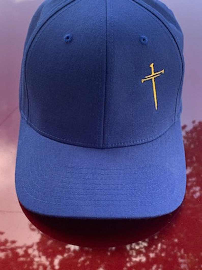 May include: A royal blue baseball cap with a gold embroidered cross on the front.
