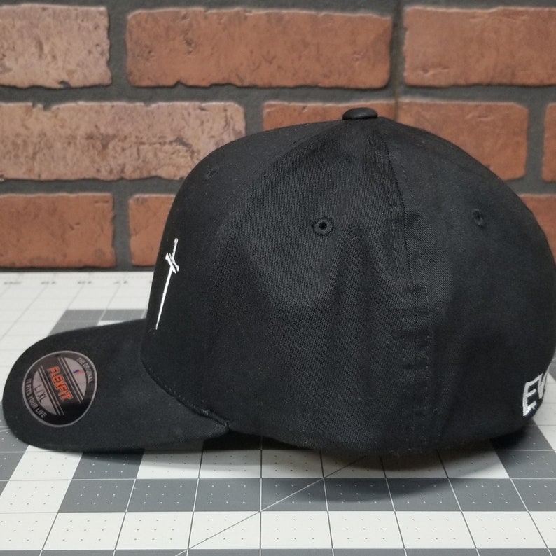 May include: A black baseball cap with a white sword design on the front. The cap has a flex fit and a black adjustable strap.