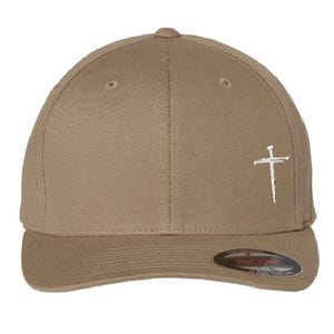 May include: A khaki baseball cap with a white embroidered cross on the front. The cap has a curved brim and a snap closure.
