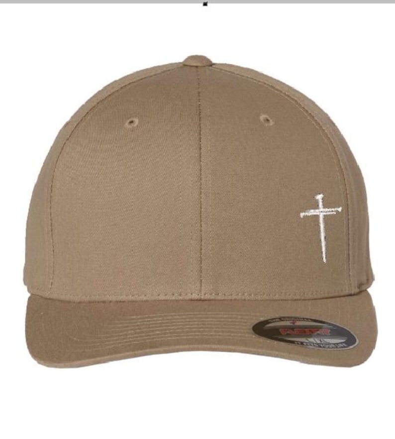 May include: A khaki baseball cap with a white embroidered cross on the front. The cap has a curved brim and a snap closure.