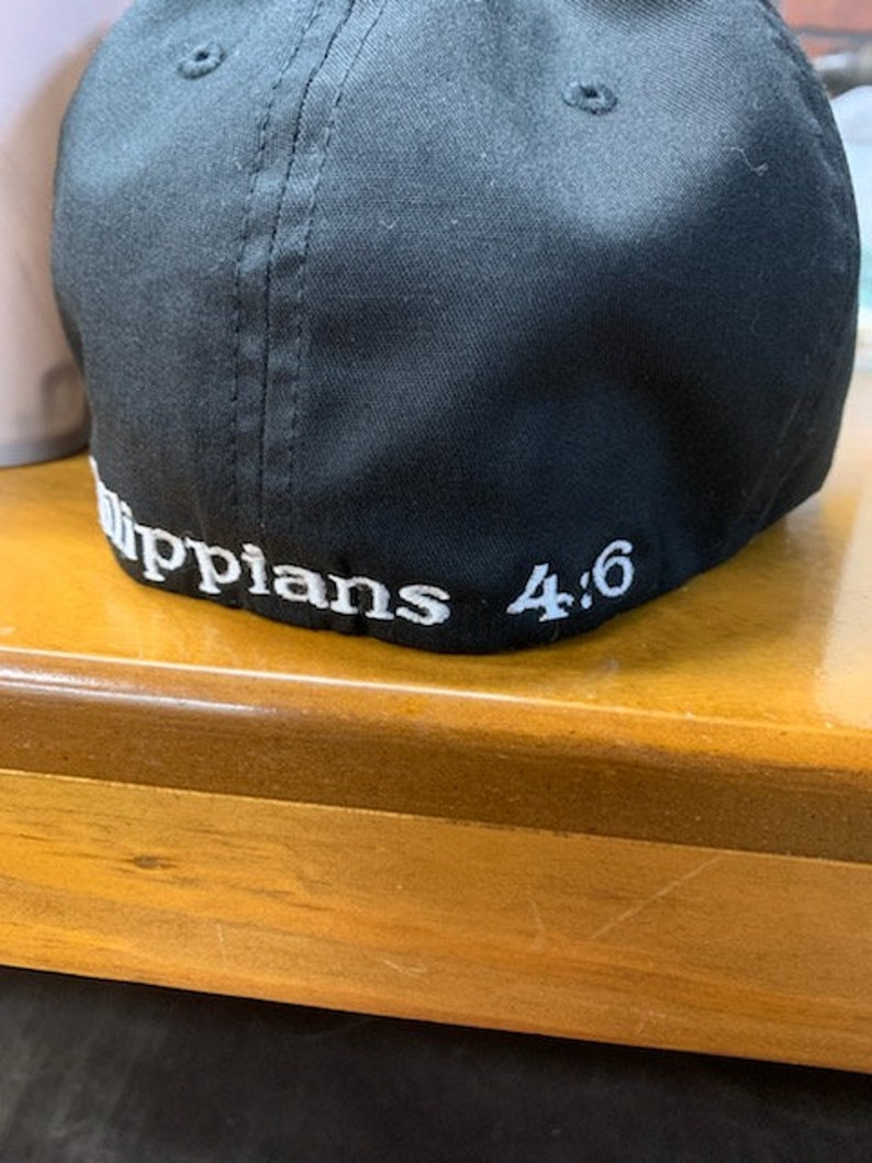 May include: Black baseball cap with white stitching and the text "Philippians 4:6" embroidered on the back.