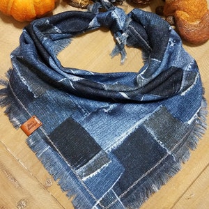May include: A blue denim scarf with a patchwork design and frayed edges. The scarf has a leather tag that reads "Bear's Boutique". The scarf is surrounded by fall-themed decorations, including a pumpkin and a scarecrow.
