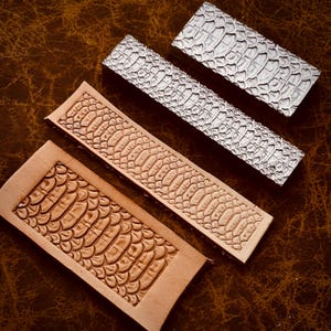 Peut inclure: Quatre pièces rectangulaires en cuir avec un motif d'écailles de reptile sont présentées sur une surface en cuir marron. Deux pièces sont marron clair, une est argentée et une est d'une couleur argentée plus foncée. Les pièces varient en taille et en forme.
