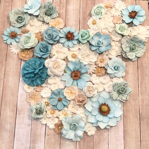 May include: A blue and white floral arrangement in the shape of a Mickey Mouse head. The flowers are made of paper and are arranged on a wooden background.