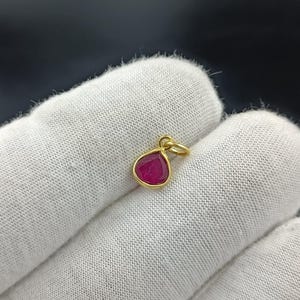 Puede incluir: Un colgante de oro con una piedra preciosa roja en forma de lágrima.