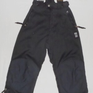 Könnte beinhalten: Schwarze Schnee-Latzhose mit gelben, verstellbaren Hosenträgern. Die Latzhose hat Reißverschlusstaschen, verstärkte Knie und Reißverschlüsse an den Knöcheln. Der Markenname "Rider Loop" ist auf dem Bein sichtbar. Für Wintersportarten.