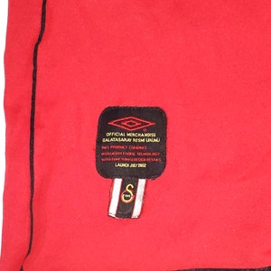 K&ouml;nnte beinhalten: Ein schwarz-wei&szlig;es Etikett mit dem Text "OFFICIAL MERCHANDISE GALATASARAY RESMİ &Uuml;R&Uuml;N&Uuml;" und "LAUNCH JULY 2002". Das Etikett ist an einem roten Shirt befestigt.