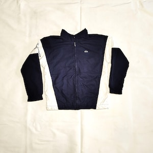以下が含まれることがあります： 胸に小さなロゴが付いた、ネイビーと白のジッパー付きジャケットです。