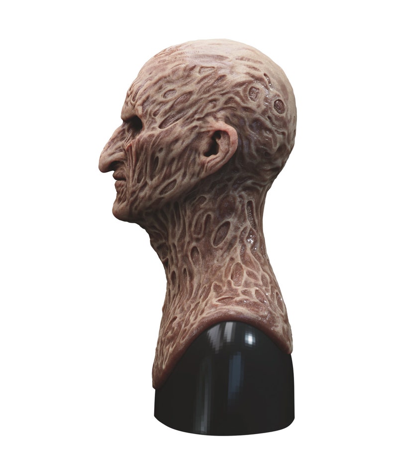 May include: A detailed, realistic, brown and beige latex mask of a monstrous, human-like creature with a textured, wrinkled face and neck. The mask is mounted on a black stand.