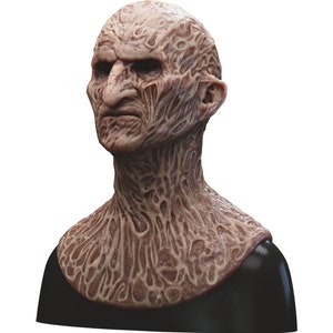 May include: A detailed, realistic, and grotesque mask of a burned human face and neck. The mask is made of a flesh-toned silicone material and features a textured surface that resembles burned skin. The mask is mounted on a black stand.