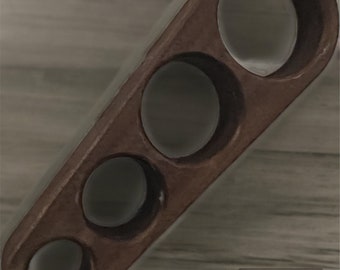May include: A wooden cigar rest with four circular openings of varying sizes. The rest is a warm brown color and has a smooth, polished finish. The design is simple and functional, suitable for holding cigars.