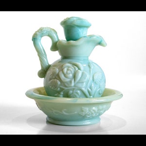 Puede incluir: Un juego vintage de jarra y cuenco de vidrio verde con un diseño de rosas. La jarra tiene un asa y un pico. El cuenco es redondo y tiene un borde festoneado.