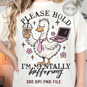 Op de afbeelding: Crèmekleurig T-shirt met een cartoon eend die een koffie en een laptop vasthoudt. De tekst luidt "PLEASE HOLD I'M MENTALLY buffering" en "300 DPI PNG FILE". Het ontwerp bevat roze accenten en bloemmotieven.