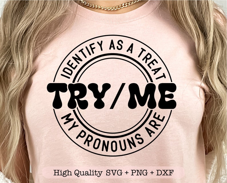 Puede incluir: Una camiseta rosa con un gr&aacute;fico circular negro que dice "IDENTIFY AS A TREAT TRY/ME MY PRONOUNS ARE". El texto est&aacute; en un estilo de fuente retro. La camiseta est&aacute; en una modelo.