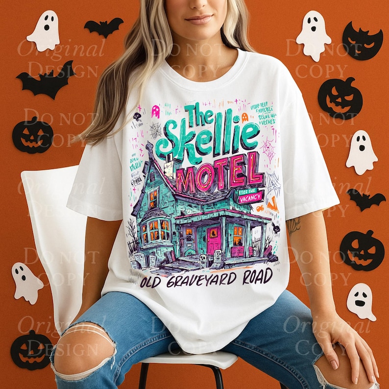 K&ouml;nnte beinhalten: Wei&szlig;es T-Shirt mit einer farbenfrohen Illustration von "The Skellie Motel", einem gruseligen Hausdesign, Spinnweben und dem Text "Old Graveyard Road". Das Design enth&auml;lt t&uuml;rkisfarbene, rosa und orangefarbene Akzente, ideal f&uuml;r Halloween.