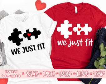 May include: Two white t-shirts with a black and white puzzle piece design and the text "We Just Fit". One shirt has a red heart in the middle of the puzzle pieces. The other shirt has a white puzzle piece design with a red heart in the middle of the puzzle pieces and the text "We Just Fit" in white.