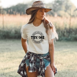 Puede incluir: Camiseta blanca con un gr&aacute;fico circular negro que dice "Identify as a treat, Try/Me, My pronouns are".