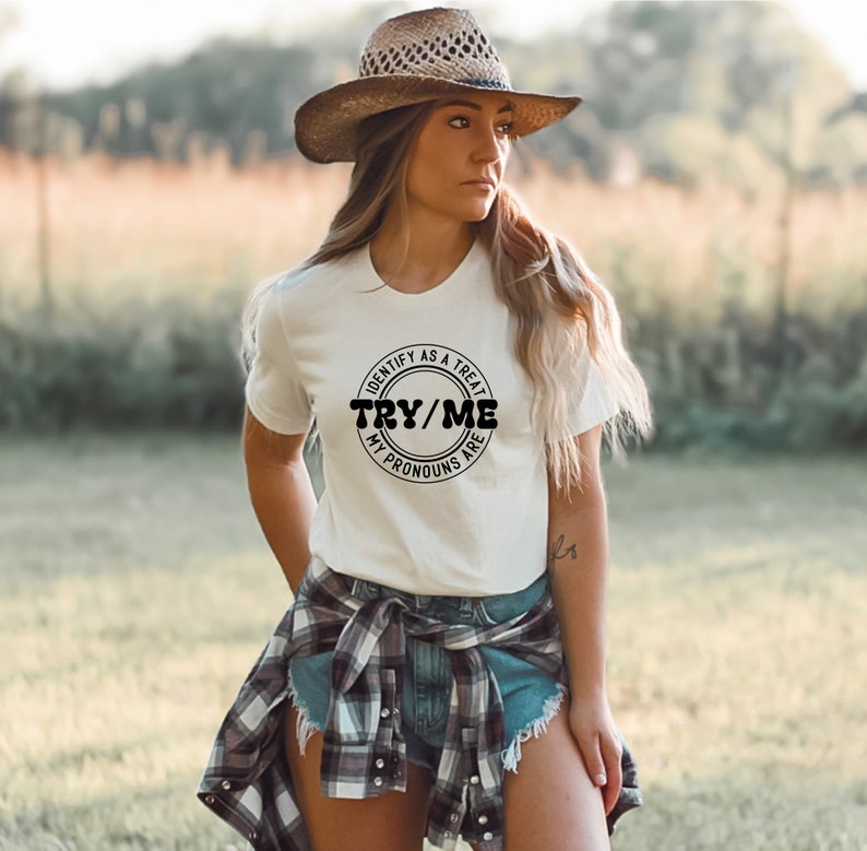 Puede incluir: Camiseta blanca con un gr&aacute;fico circular negro que dice "Identify as a treat, Try/Me, My pronouns are".