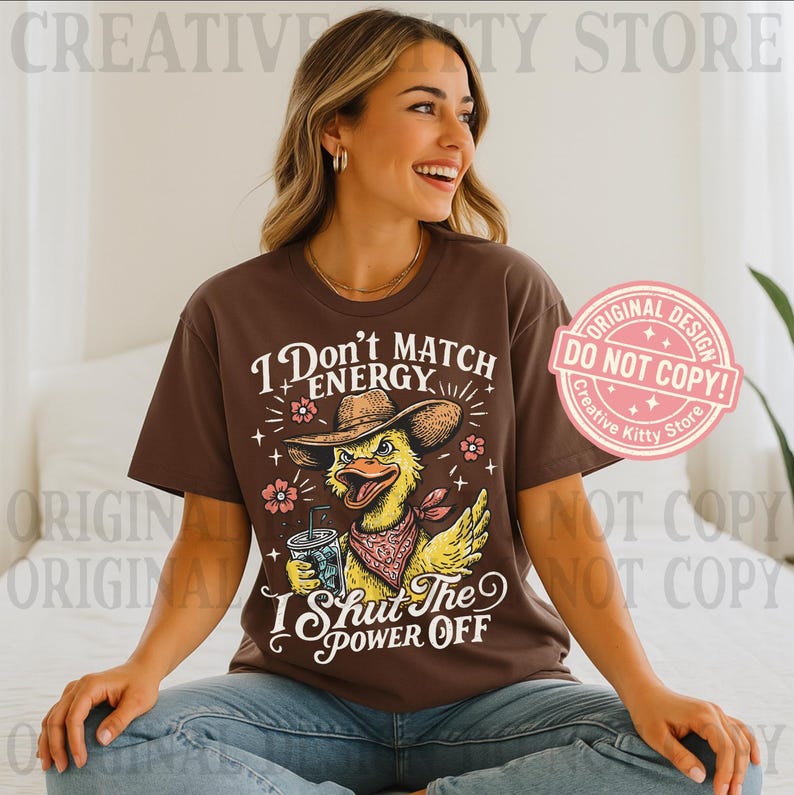 May include: Brown t-shirt with the text "I Don't Match Energy, I Shut The Power Off" and a cartoon duck wearing a cowboy hat and bandana. The duck is holding a beverage. The shirt has a round neck and short sleeves.