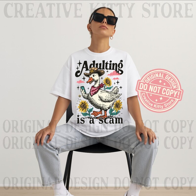 May include: White t-shirt featuring a cartoon duck in a cowboy hat and bandana, with sunflowers. The text "Adulting is a scam" is printed below the duck. A pink stamp reads "Original Design Do Not Copy!" in a circle.