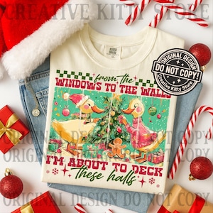 Puede incluir: Camiseta color crema con un dise&ntilde;o de patos navide&ntilde;os. El gr&aacute;fico presenta dos patos decorando un &aacute;rbol de Navidad, con el texto "from the windows to the walls, I'm about to deck these halls." La imagen est&aacute; rodeada de adornos navide&ntilde;os.