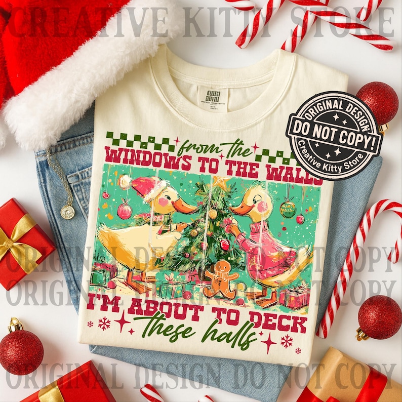 Puede incluir: Camiseta color crema con un dise&ntilde;o de patos navide&ntilde;os. El gr&aacute;fico presenta dos patos decorando un &aacute;rbol de Navidad, con el texto "from the windows to the walls, I'm about to deck these halls." La imagen est&aacute; rodeada de adornos navide&ntilde;os.