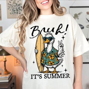 May include: White t-shirt with a graphic of a duck wearing sunglasses and a floral shirt, holding a surfboard. The text "Bruh! It's Summer" is printed below the duck.