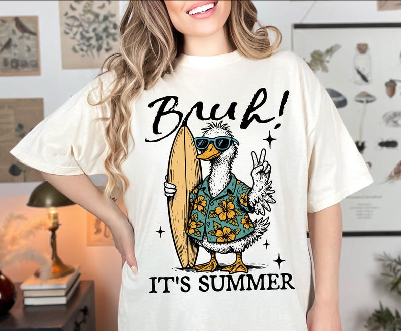 May include: White t-shirt with a graphic of a duck wearing sunglasses and a floral shirt, holding a surfboard. The text "Bruh! It's Summer" is printed below the duck.