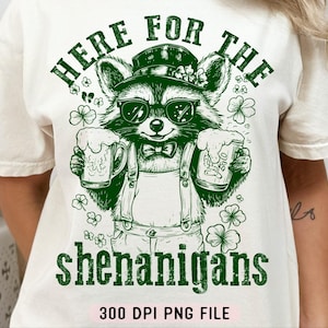 Puede incluir: Una camiseta blanca con un gr&aacute;fico de mapache verde sosteniendo dos jarras de cerveza verdes. El texto "Here for the shenanigans" est&aacute; impreso en verde debajo del mapache. El texto "300 DPI PNG FILE" est&aacute; impreso en negro en la parte inferior de la camiseta.