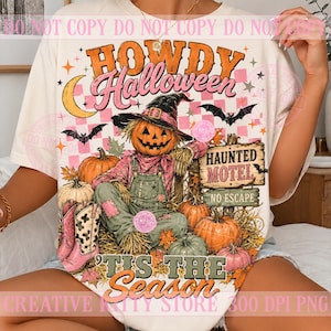Puede incluir: Una camiseta color crema con un gráfico de un espantapájaros con cabeza de calabaza y sombrero de bruja, rodeado de calabazas, murciélagos y botas vaqueras rosas. El texto dice Howdy Halloween y Tis The Season con un letrero de Haunted Motel.